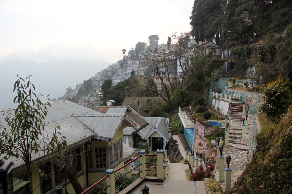 Aerial view of Darjeeling Valley showcasing lush greenery, winding roads, and the Himalayan mountain range under a clear sky from our Best Homestays in Darjeeling